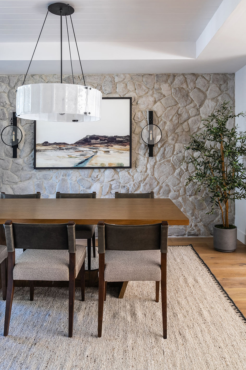dining area with stone accent wall and large circular light fixture over a wood table