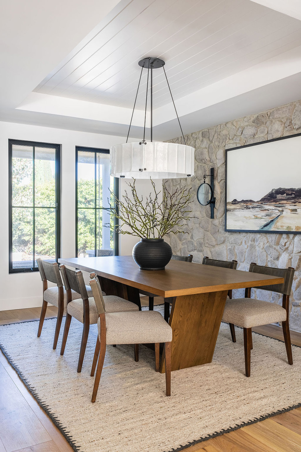 dining area with stone accent wall and large circular light fixture over a wood table