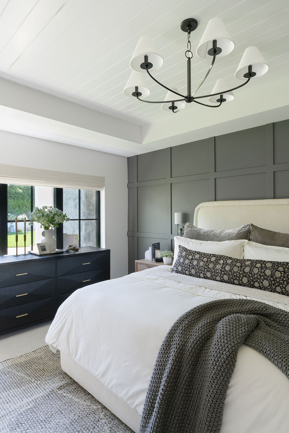bedroom design with dark gray accent wall, black hanging chandelier, and neutral bedding colors