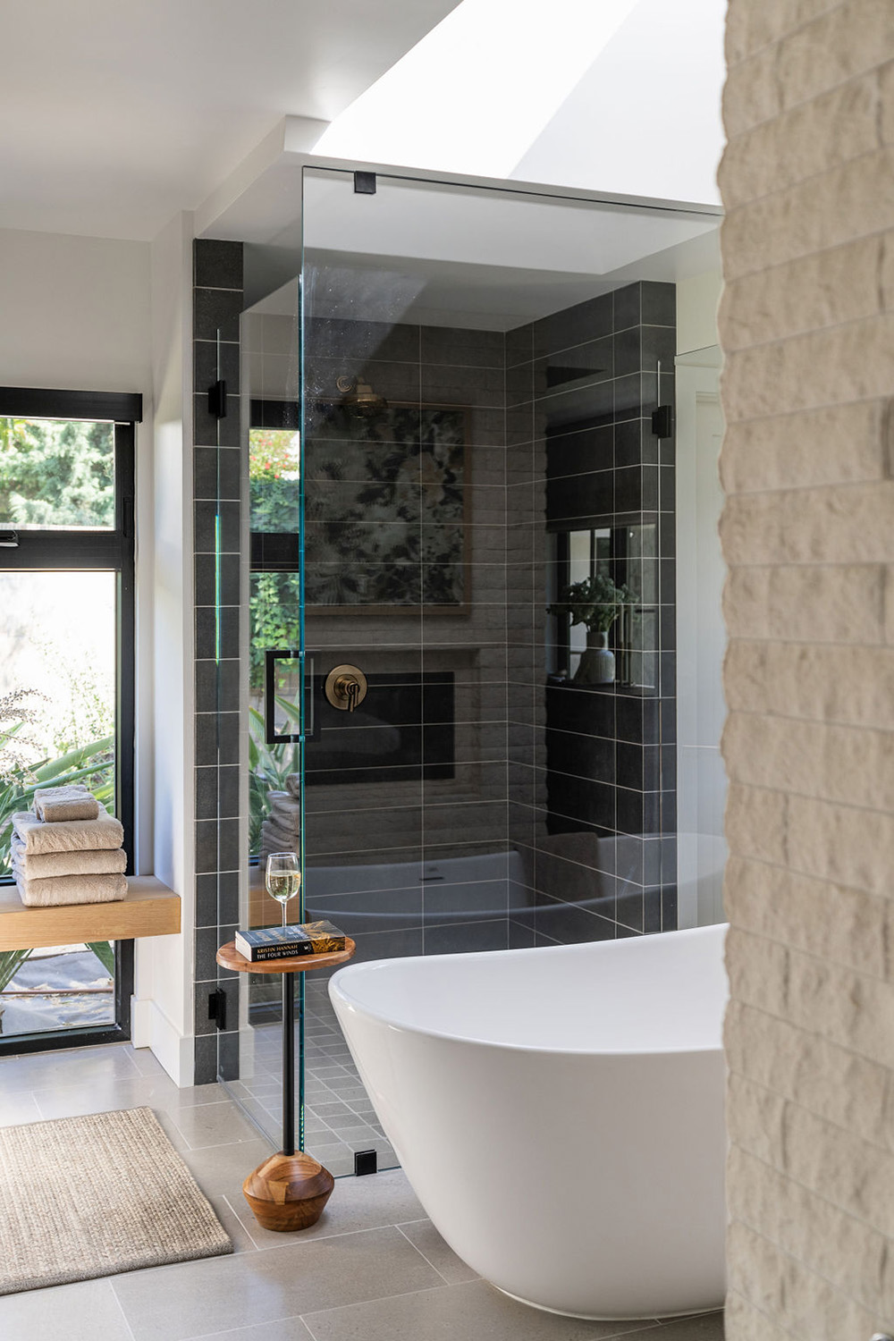 modern bathroom design with standing tub, dark shower tile and stone accent wall
