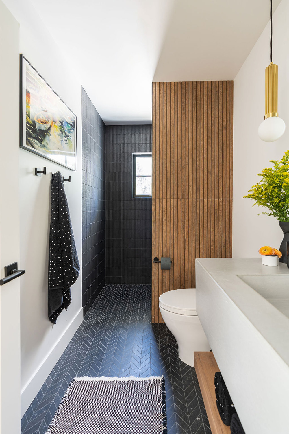 bathroom design with dark gray shower tiles, wood accent wall and herringbone floor tile