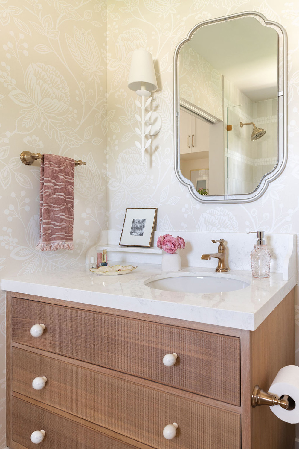 bathroom design with light neutral floral wallpaper, scalloped mirror and wood vanity