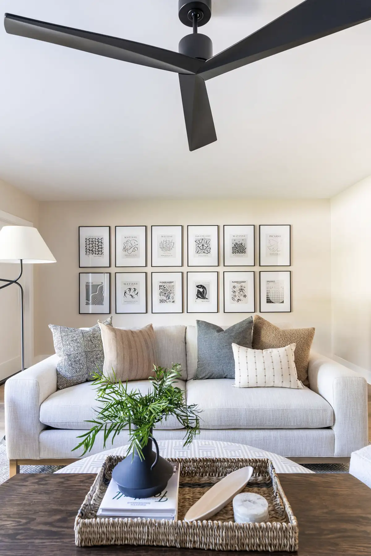 Interior design of a living room with 12 pieces of artwork on the wall behind a light couch with neutral colored pillows and a natural wood coffee table